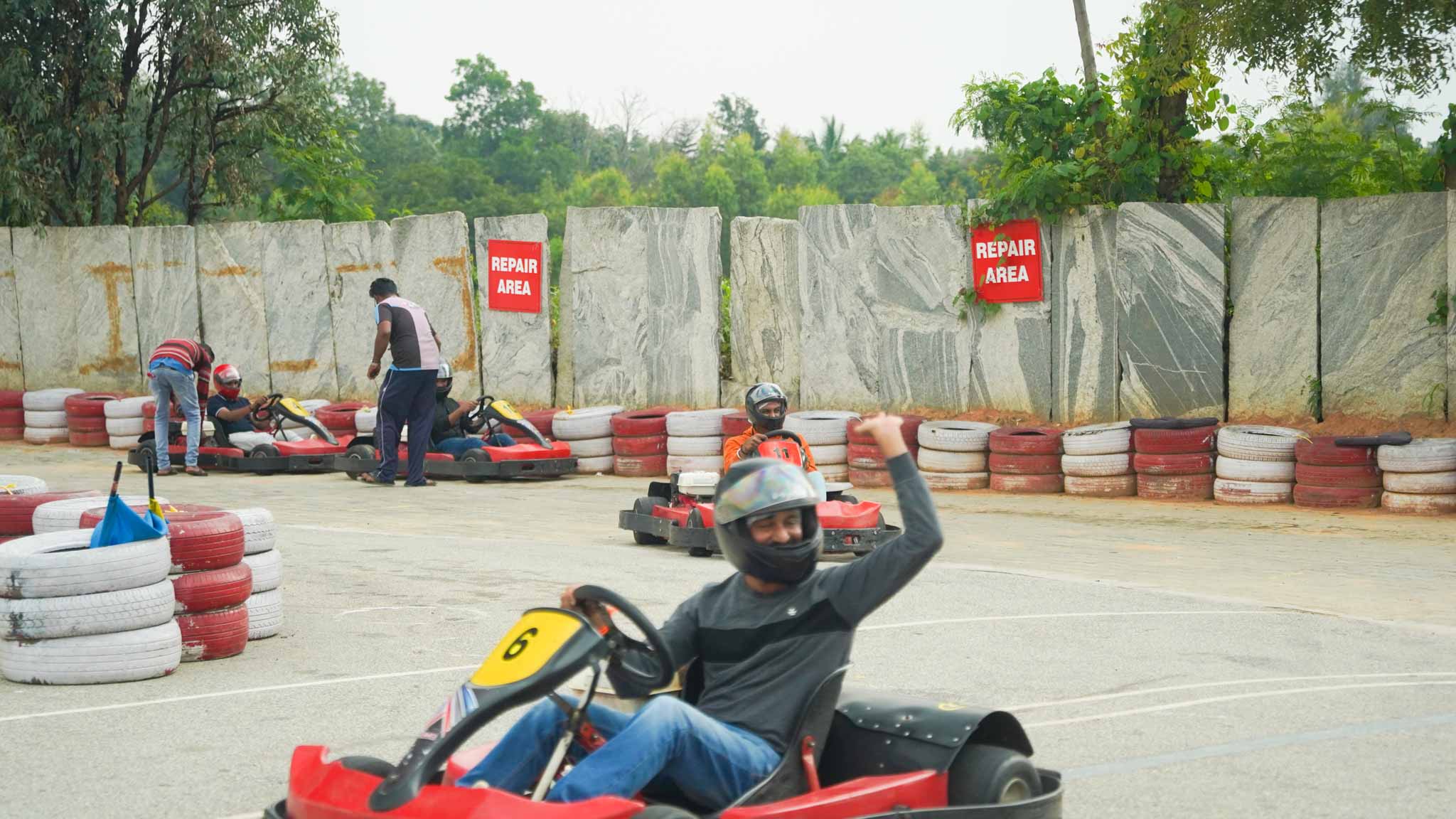A go-kart driver in the repair area, raising a hand in celebration.